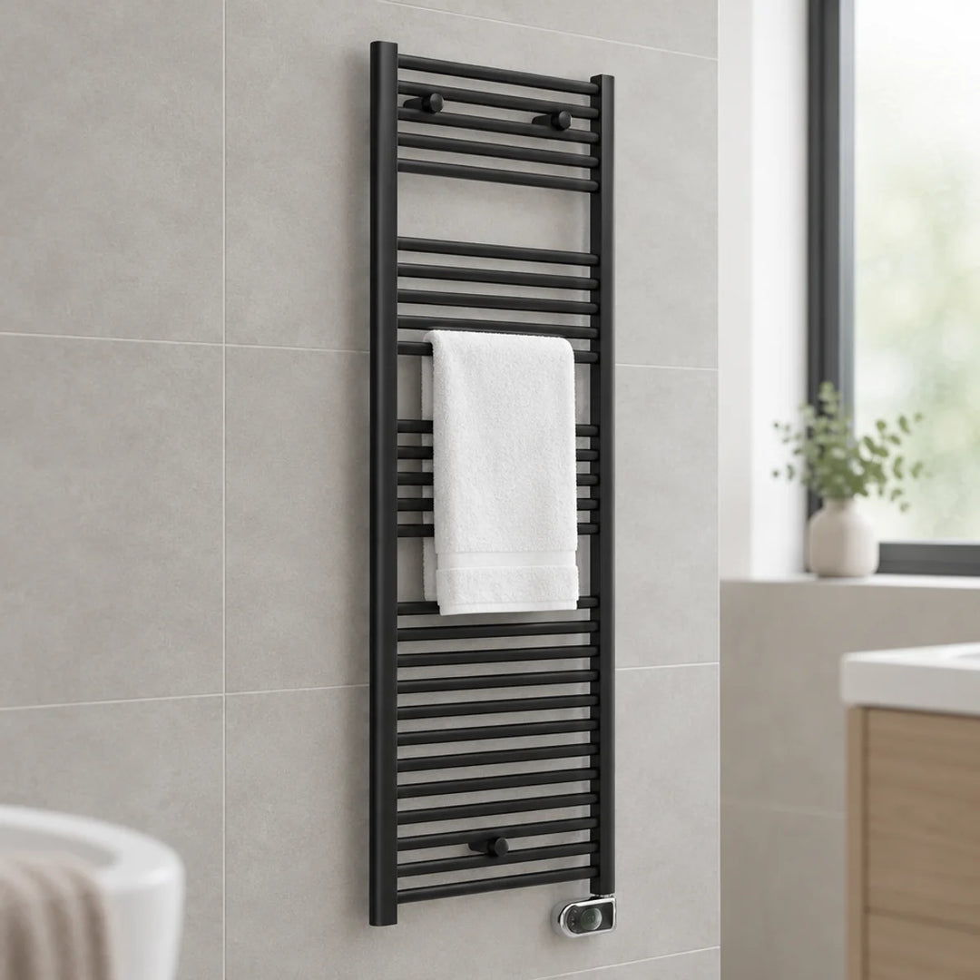Essential Electric ERP black heated towel rail with a white towel, wall-mounted on grey tiles in a bathroom with window and vanity