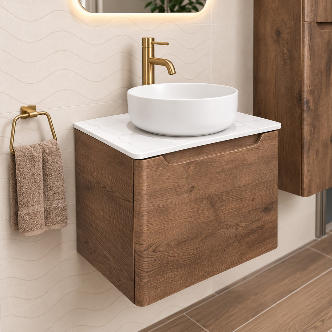 A modern wall-mounted bathroom vanity with a wood-grain cabinet, white marble-look top, white vessel sink, and a gold faucet, shown in a styled bathroom setting with a towel and mirror.