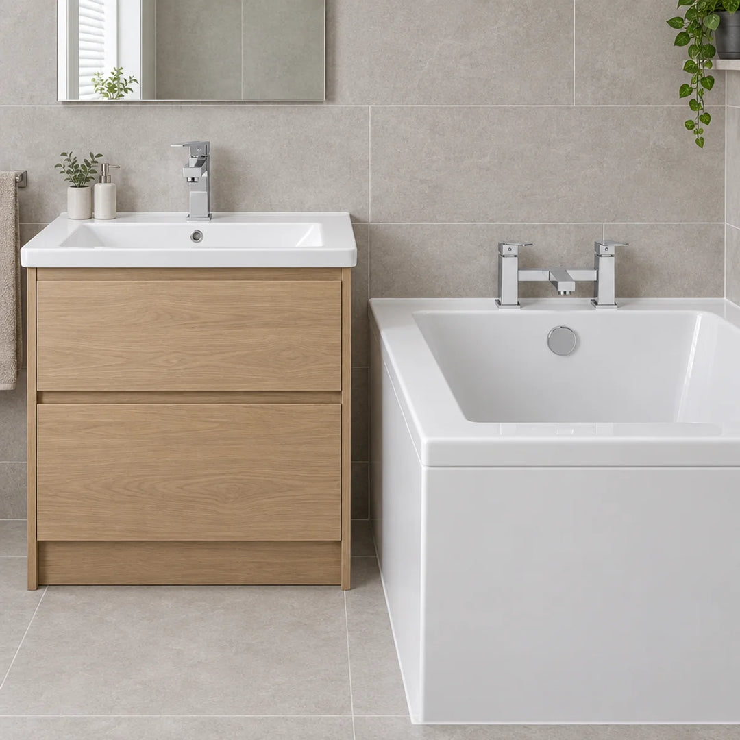 Tre Mercati Haworth chrome bath filler and basin mixer taps shown beside an oak vanity unit and white bath in a grey tiled bathroom