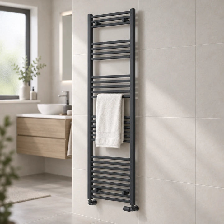 Capo anthracite flat towel rail mounted on a beige tiled bathroom wall with a white towel, wooden vanity unit and basin behind