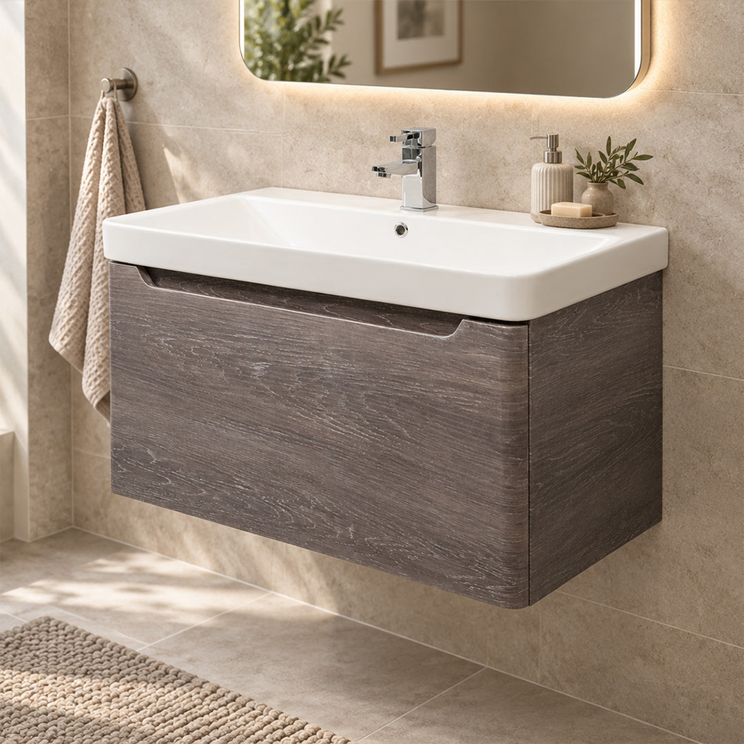 A modern wall-mounted bathroom vanity with a white rectangular sink and a dark wood-grain cabinet, shown installed against a beige tiled wall with a mirror, towel, and small decor items.