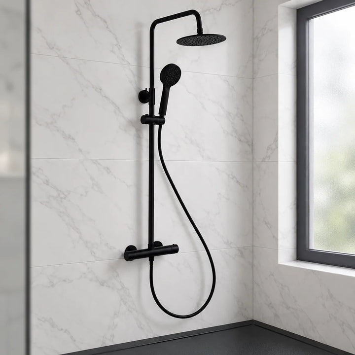 Rotunda round matt black thermostatic shower set with rainfall head and handset, installed on white marble-effect tiles beside a window