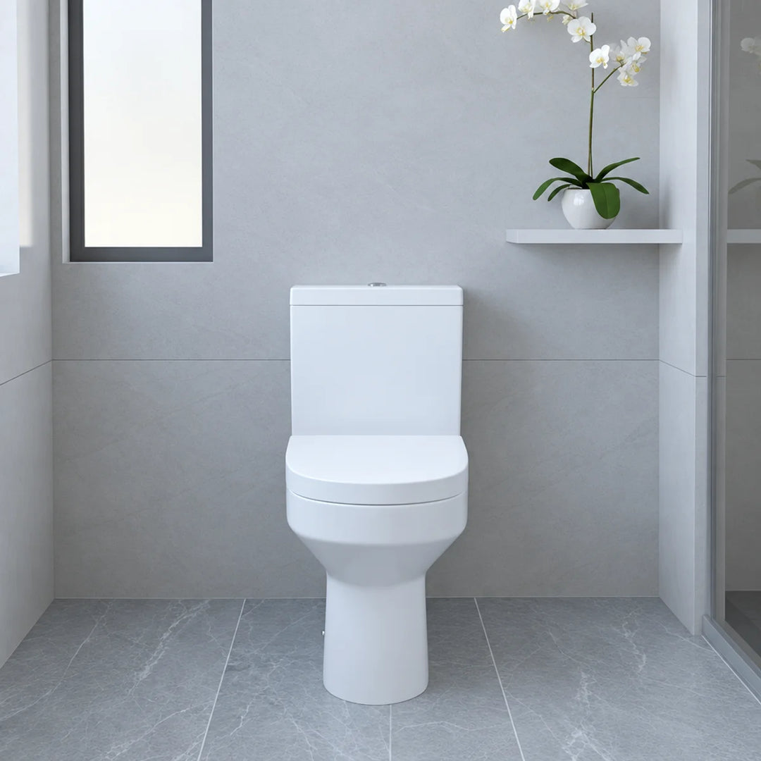 Harmony white close coupled back to wall toilet with soft close seat, front view in a grey tiled bathroom with orchid on shelf