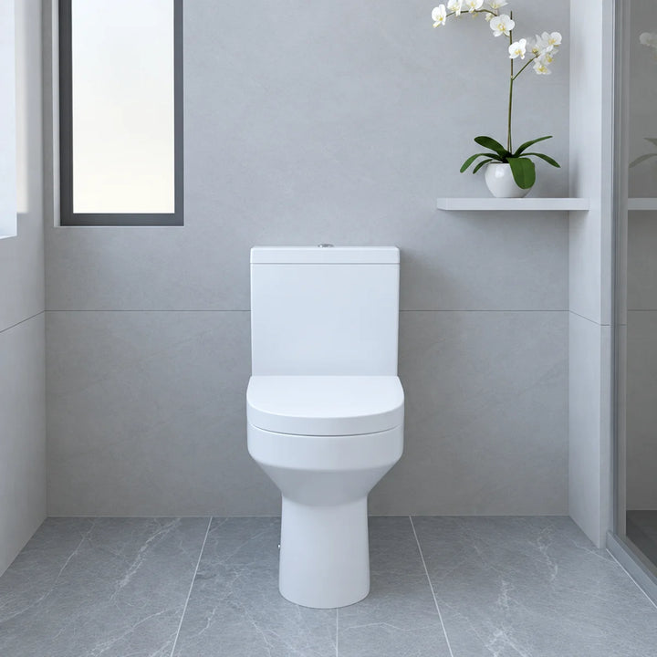 Harmony white close coupled back to wall toilet with soft close seat, front view in a grey tiled bathroom with orchid on shelf
