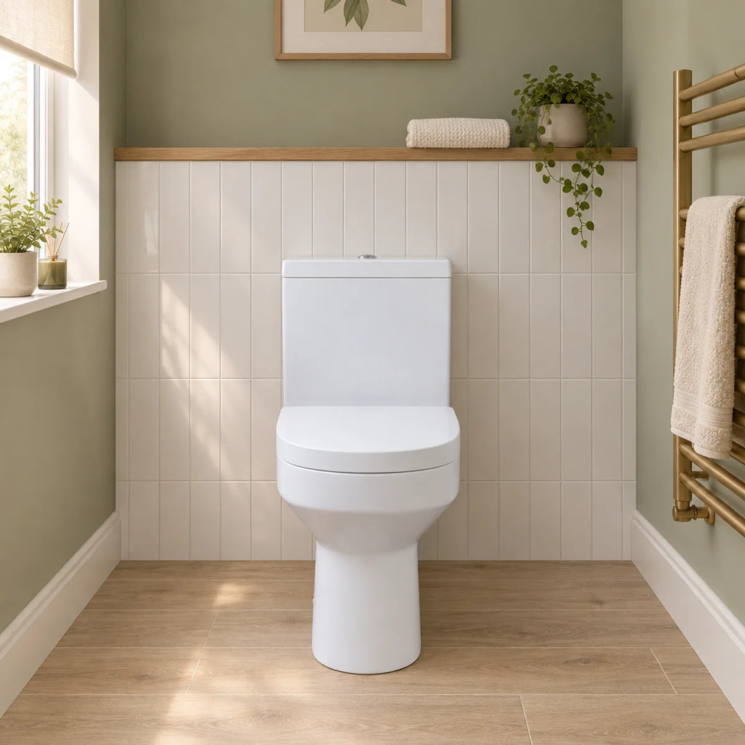 Harmony rimless close coupled toilet in white with soft close seat, front view in a sage green cloakroom with cream tiles and brass towel radiator