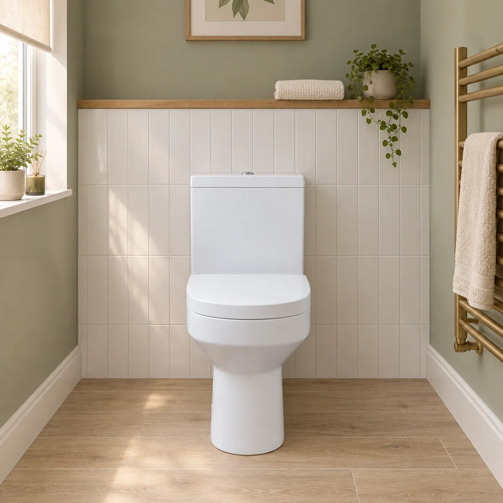 Harmony rimless close coupled toilet in white with soft close seat, front view in a sage green cloakroom with cream tiles and brass towel radiator