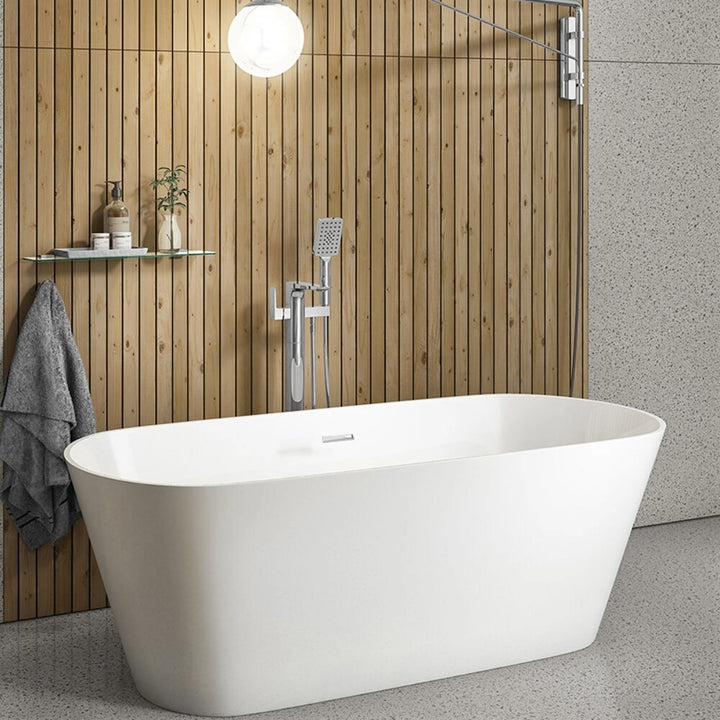 A modern freestanding bathtub in white, positioned in a bathroom with a light wood slat wall, chrome shower fixture, floating shelf, and gray speckled floor.