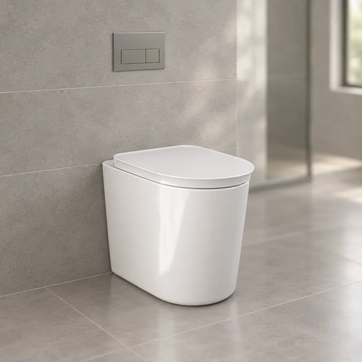 RAK Ceramics Valet soft close seat in gloss white on a back to wall toilet, shown in a bathroom with grey tiles and a chrome flush plate
